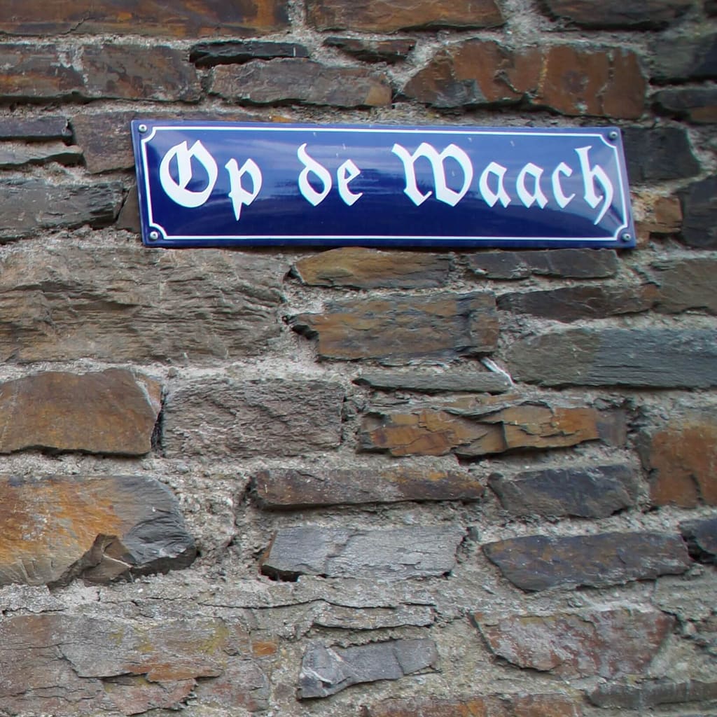 Ein Straßenschild mit der Aufschrift "Op de Waach" auf einer Steinmauer.